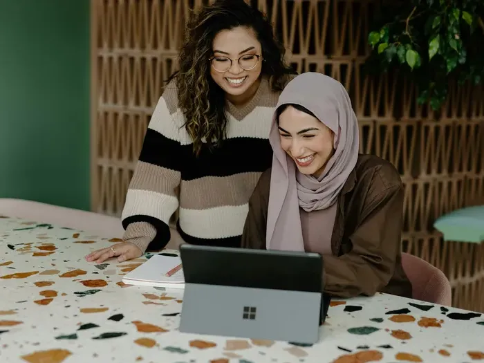 Two women smiling at a laptop while updating a local business listing via City Service Connect to improve reach
